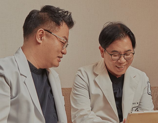 흰 가운 의사 두 명이 태블릿을 보며 웃는 모습