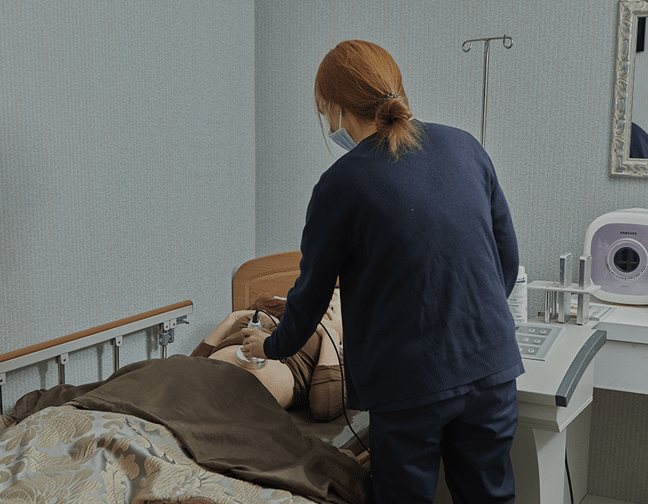 간호사가 침대에 누운 환자에게 초음파 관리를 하는 모습
