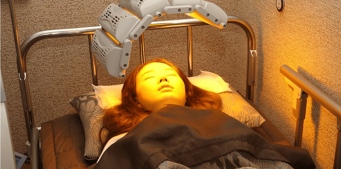 침대에 누운 여성 얼굴 위 LED 관리 장비